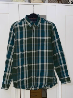 Grön och blå rutig skjorta - Snygg rutig skjorta i grönt, blått och vitt med klassisk krage och knappar framtill. Skjortan har lång ärm och bröstficka på vänster sida. Perfekt för dig som gillar en avslappnad men ändå stilren look.