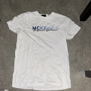 Vit McKenzie t-shirt med brodyr - Vit t-shirt från McKenzie med broderad logga i blått och ljusblått på bröstet. Klassisk passform och rund halsringning. Tillverkad i mjuk bomull för en skön känsla. Perfekt för en avslappnad och sportig stil . Har en liten fläck