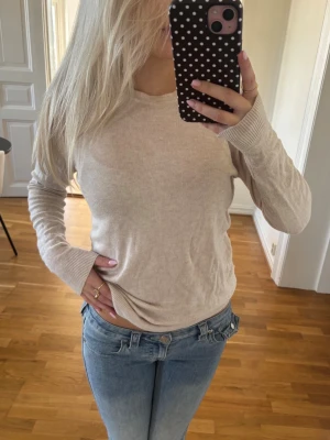 Beige stickad tröja - Säljer en enkel och stilren beige stickad tröja med rund hals och långa ärmar. Tröjan har ribbade muddar vid ärmslut och nederkant, vilket ger en snygg passform. Perfekt att matcha med jeans för en avslappnad look. Skriv för mer info💕