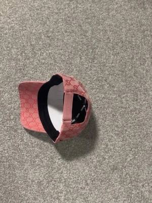 Rosa GG keps med GG-mönster - Säljer en rosa keps från GG med klassiskt GG-monogram i rött över hela kepsen. Kepsen har böjd skärm, justerbar rem bak och gröna/röda detaljer på sidorna. Materialet är canvasliknande tyg som känns både lyxigt och tåligt. Perfekt för dig som vill sticka ut.