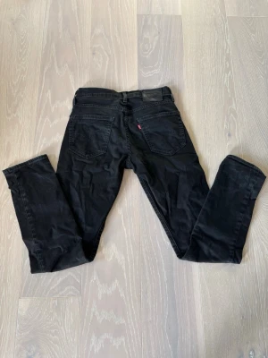 Svarta Levis 502 - Säljer ett par svarta jeans med rak passform och klassisk femficksdesign. Jeansen har bälteshällor, knappgylf och är tillverkade i ett mjukt denimtyg. Perfekta för en avslappnad och stilren look. Modellen är 502 i tapered fit. Vid intresse eller frågor är det bara att höra av sig. 