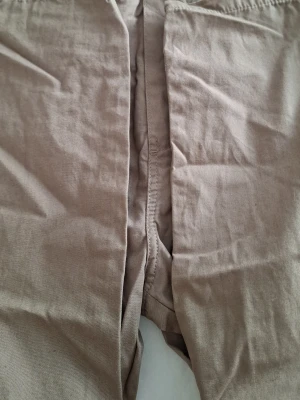 Beiga byxor med resårmidja - Säljer ett par beiga byxor med resår i midjan. Byxorna är tillverkade i ett mjukt och stretchigt material som känns skönt mot huden. Perfekta för chill dagar hemma eller när du vill ha det extra bekvämt.