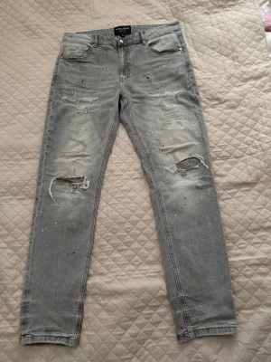 Supply and demand  - Säljer ett par grå skinny jeans med slitningar och hål på båda benen. Jeansen har fem fickor och en tvättad look med små färgstänk för en trendig vibe. Perfekta för dig som gillar streetstyle och vill ha ett par jeans med attityd.  Storlek XL - passar dig som är 180-186 cm och 75-85kg.