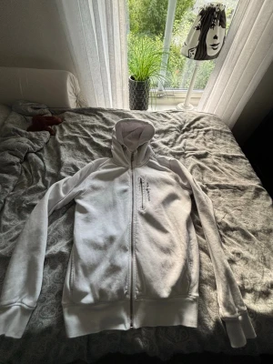 Vit hoodie med dragkedja och huva - Priset kan diskuteras!Säljer en vit hoodie med dragkedja framtill och huva. Hoodien har långa ärmar, ribbade muddar och en diskret textdetalj på bröstet. Perfekt för en avslappnad och stilren look. Materialet känns mjukt och bekvämt.