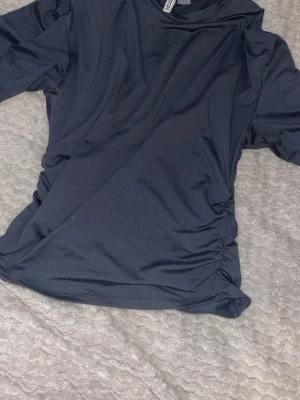 Topp från H&M - Snygg mörkblå topp från Divided H&M i stretchigt material. Toppen har lätt rynkade sidor 