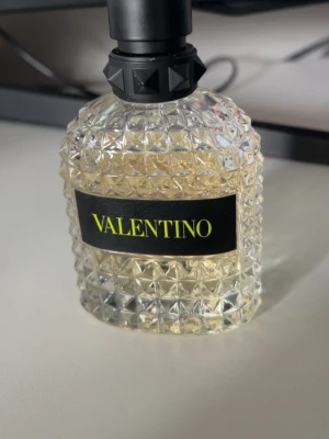 Valentino parfym i kristallflaska - Exklusiv parfym från Valentino i en transparent, kristallmönstrad glasflaska med svart etikett och gul text. Flaskan har en svart, dekorativ kork med nitar som ger en lyxig känsla. Perfekt för dig som gillar eleganta och trendiga dofter.