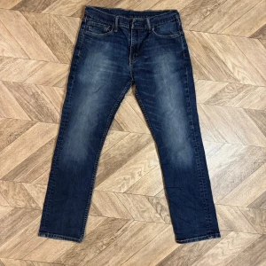 Levis 511  - Säljer ett par mörkblå jeans med raka ben och snygga slitningar framtill. Jeansen har klassisk femficksdesign och normal midja. Materialet är denim i bomull med lite stretch för extra komfort. Perfekta till en avslappnad stil.