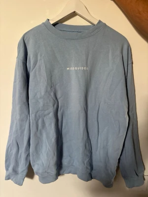 Blå sweatshirt från Missguided - Ljusblå sweatshirt från Missguided med rund halsringning och tryckt logga på bröstet. Tröjan har en avslappnad passform, långa ärmar och ribbade muddar vid ärmslut och nederkant. Perfekt för en chill och casual look.