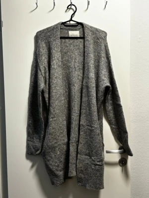 Samsøe Samsøe Nor Cardigan Gråmelerad S - Säljer en Samsøe Samsøe Nor cardigan 7355 i Grey Mel. Gråmelerad långkofta, oversize S som passar S-L. Öppen med fickor, supermjuk ullblandning. Mycket fint skick, endast en liten lös tråd vid ena fickan, se bild. Annars inga fel. 399kr (frakt ca 79kr tillkommer). Säljer då jag rensar.