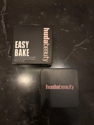Huda Beauty Easy Bake Cupcake puder - Loose baking & setting powder från Huda Beauty i nyansen Cupcake. Kommer i en fyrkantig svart burk med rosa text och matchande kartong. Perfekt för att fixera foundation och ge en matt finish. Innehåller 20 g.