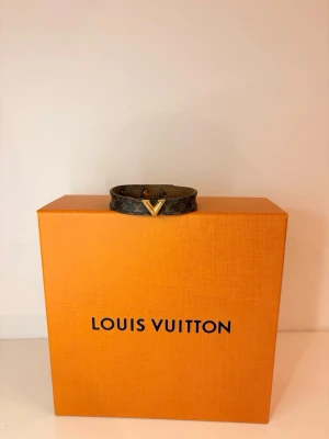 Louis Vuitton monogram armband - Snyggt armband från Louis Vuitton i klassiskt brunt monogrammönster med guldfärgad V-detalj framtill. Tillverkat i läder med tryckknappsstängning. Perfekt accessoar för att lyfta din outfit med en lyxig touch. Säljer detta armband ! Lite slitet, därav priset! Men asså älskar detta armband så mkt, stylar upp varenda outfitt man har, köpt snabbt o smidigt 
