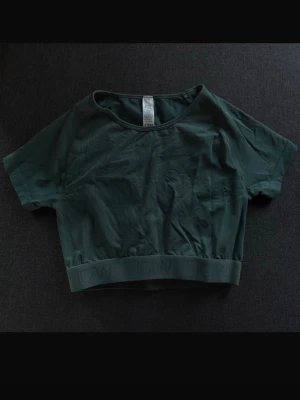 Tealfärgad croppad topp från ICANIWILL - Snygg mörkgrön croppad topp från ICANIWILL med korta ärmar och bred resår nedtill. Tillverkad i återvunnen nylon och spandex för en stretchig och bekväm känsla. Perfekt till träning eller chill outfits. Testad men aldrig använd.