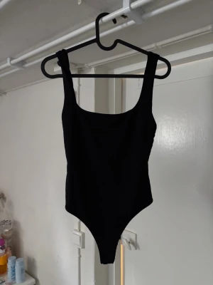 Svart body  - Enkel och stilren svart body med breda axelband och rundad urringning både fram och bak. Modellen är figurnära och har en klassisk skärning. Jättesnyggt med kostymbyxor! 