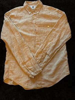 Beige linneskjorta med knappar - Snygg beige skjorta i linne med klassisk krage och långa ärmar. Skjortan har knäppning framtill och en bröstficka. Perfekt för en avslappnad men stilren look.