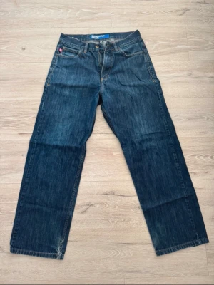 Mörkblå raka jeans - Säljer ett par mörkblå jeans med rak passform och klassiska kontrastsömmar. Jeansen har fem fickor och knappgylf. Perfekta för en avslappnad och stilren look.