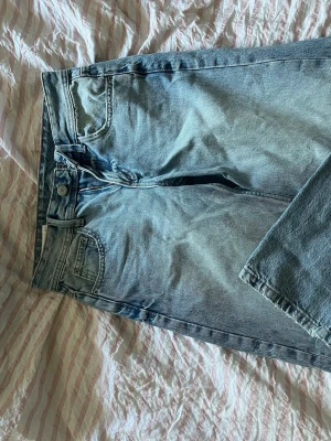 Ljusblå raka jeans från Pull&Bear - Säljer ett par ljusblå jeans från Pull&Bear med rak passform och klassisk femficksdesign. Jeansen har hög midja, dragkedjegylf och är tillverkade i denim. Perfekta för en avslappnad och trendig look.