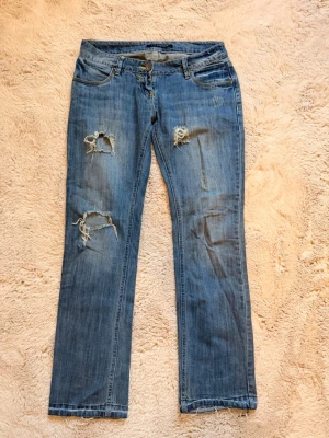 Blå slitna jeans med raka ben - Säljer ett par blå jeans med raka ben och slitna detaljer på låren och knäna. 