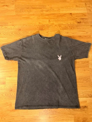 Svart t-shirt med Playboy-logga - Cool svart playboy t-shirt med tvättad look och en liten rosa Playboy-kanin broderad på bröstet. Klassisk rund hals och korta ärmar. Perfekt för dig som gillar streetwear stil.        Använt fåtal gånger…