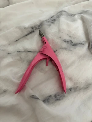 Rosa tip cutter för naglar - Praktisk rosa tip cutter för naglar, perfekt för att klippa lösnaglar eller tippar till önskad längd och form. Handtaget är ergonomiskt utformat i metall och klippdelen är i metall för precision. Enkel att använda för både nybörjare och proffs.
