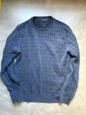 Blå kabelstickad tröja Tommy Hilfiger - Snygg blå kabelstickad tröja från Tommy Hilfiger i storlek M. Tröjan har rund halsringning, ribbade muddar och klassiskt flätmönster. Perfekt för dig som gillar stilrena och tidlösa plagg i garderoben.