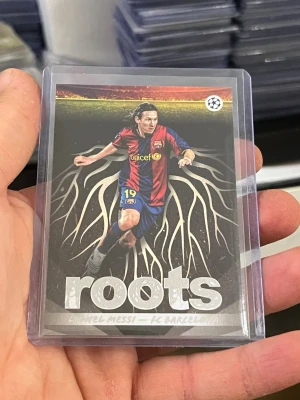 Samlarbild Lionel Messi Roots - Unik samlarbild från Topps med Lionel Messi i Barcelona-tröja, del av 'roots'-serien. Kortet har färgstark design med rötter i bakgrunden och är skyddat i plastficka. Perfekt för dig som älskar fotboll och samlarkort.