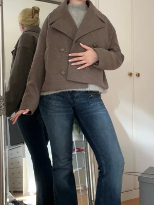 Brun ullkappa  - Snygg kort brun kappa i ullblandning med bred krage och dubbelknäppning framtill. Modellen är boxig och har långa ärmar, perfekt för en trendig och avslappnad look. Passar till jeans eller kjol för en cool stil. Aldrig andvänd💕