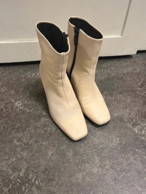 Beiga stövletter med fyrkantig tå - Snygga beiga stövletter med högre skaft och fyrkantig tå. Dragkedja på insidan och klack för extra höjd. Utsidan ser ut att vara i slätt material, troligen syntet eller läder. Perfekta för att lyfta din outfit. Dem är enbart provade 