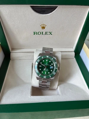 Submariner  - Ny Green Submariner med alla original tillbehör. 40 mm urtavla med nattbelysning, självlysande stenar och datumfönster. Högkvalitativt urverk med Oyster-spänne. Köpt för 420 euro. Perfekt för den som älskar lyxiga accessoarer. Levereras med ask och tillbehör.