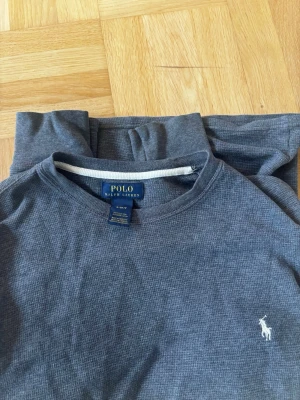 Grå sweatshirt från Polo Ralph Lauren - Säljer en stilren grå hoodie från Polo Ralph Lauren i 100% bomull. Klassisk design med huva och den ikoniska vita logon broderad på bröstet. Perfekt för dig som gillar en enkel men snygg look. Passar till det mesta och är superbekväm.
