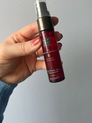 Rituals The Ritual of Ayurveda mist - En elegant hår- och kroppsmist från Rituals i serien The Ritual of Ayurveda. Flaskan är cylinderformad och har en djup röd färg med svart spraymunstycke och genomskinligt lock. Perfekt att spraya i håret eller på kroppen för en fräsch doft.