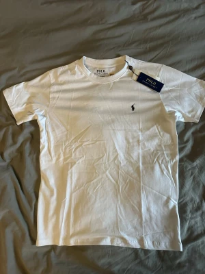 Vit slim fit t-shirt från Polo Ralph Lauren - Klassisk vit t-shirt från Polo Ralph Lauren i slim fit-modell. Tillverkad i mjuk bomull och har korta ärmar samt den ikoniska lilla broderade loggan på bröstet. Perfekt basplagg för en clean och stilren look.