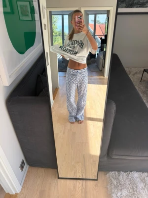 Blåvita pyjamasbyxor med mönster - Säljer ett par pyjamasbyxor i blått och vitt med ett snyggt grafiskt mönster. Byxorna har rak passform och resår i midjan för extra komfort. Perfekta för mysiga hemmakvällar eller lata morgnar.