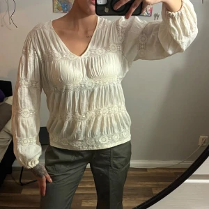 Vit boho-blus med spetsdetaljer - Säljer en vit boho-inspirerad blus från Vila med v-ringning och romantiska spetsdetaljer. Blusen har långärmade puffärmar och ett luftigt, avslappnat fall. Perfekt för dig som gillar en feminin och trendig stil.