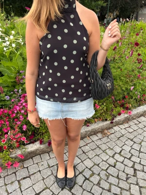 Svart prickig halterneck topp - Helt ny!!!        Säljer en svart halterneck topp med mint prickar. Toppen är ärmlös och har öppen rygg med knyt i nacken. Perfekt för dig som gillar en cool och trendig look. Materialet känns lätt och luftigt, perfekt för varma dagar.
