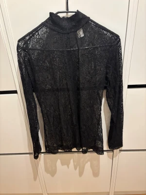 Svart spetsblus med polokrage - Säljer en svart långärmad spetsblus med polokrage. Blusen är helt genombruten i spets och har en tight passform som ger en snygg siluett. Perfekt att styla lager på lager eller med ett linne under för en trendig look.