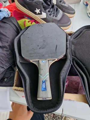 Bordtennisracket med fodral - Säljer ett bordtennisracket med svart och röd gummiyta, handtag i trä och medföljande svart fodral med dragkedja. Perfekt för dig som vill spela pingis med kompisarna. Racketen har en klassisk form och greppvänligt handtag.