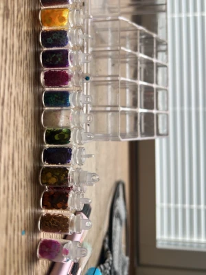 Nageldekorationer och glitterpulver - Säljer ett set med små flaskor fyllda med nageldekorationer i olika färger och former, perfekt för att skapa unika nageldesigner. Medföljer även tre burkar med glitterpulver i beige, rosa och nude nyanser. Passar dig som vill experimentera med kreativa nagellooks.