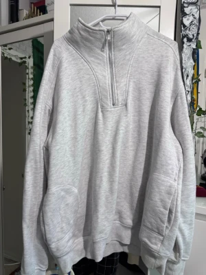Ljusgrå halvzip hoodie från Primark - Ljusgrå hoodie från Primark i storlek Large. Tröjan har halv dragkedja framtill, hög krage och stora fickor på sidorna. Tillverkad i mjukt sweatshirtmaterial som är perfekt för chill dagar. Enkel och clean design som passar till det mesta.