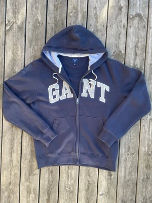 GANT Zip Up Hoodie – Marinblå | Strl XL - Säljer en stilren marinblå zip up-hoodie från GANT i storlek XL. En clean och tidlös modell med GANT-logga framtill och en klassisk marinblå färg som är enkel att matcha med resten av garderoben. Den mjuka känslan, luva och dragkedja framtill gör den perfekt både till vardags och när du vill ha något enkelt men snyggt på dig. En mångsidig hoodie som funkar till många olika outfits och tillfällen.
