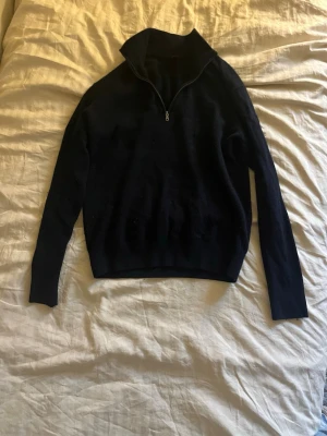 Marinblå Kashmir halv zip - En stilren mörkblå tröja med halv dragkedja och hög krage. Tröjan har långa ärmar och är tillverkad i ett mjukt, tunt material som passar perfekt för lager på lager. Enkel och klassisk design som funkar till det mesta.