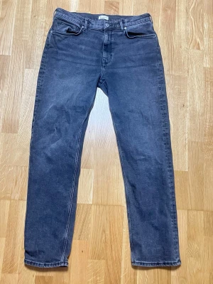 Mörk gråa/svarta jeans från Gant - Säljer ett par mörk gråa/svarta jeans från GANT med rak passform och klassisk femficksdesign. Jeansen har en stilren look och är tillverkade i ett mjukt denimtyg som känns bekvämt hela dagen. Perfekta till en avslappnad outfit.