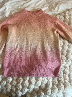 Stickad tröja i rosa och beige ombre - Mysig stickad tröja med ombre-effekt i rosa/coral/beige toner. Tröjan har rund halsringning, långa ärmar och ribbade muddar vid ärmslut och nederkant. Perfekt för dig som gillar mjuka färgövergångar och en avslappnad stil.                            Passar någon i xxs-s möjligen M om man gillar tjocktröjor lite tajtare. Är dock i 146-152 i barn storlek. Är i väldigt bra skick för utom en fläck som jag visar på bilden syns knappast.