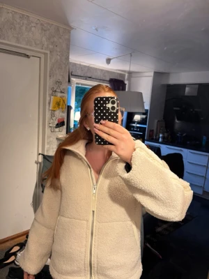 Krämvit teddyjacka med dragkedja - Mysig krämvit teddyjacka med hög krage och dragkedja framtill. Jackan har en oversized passform och är gjord i fluffigt teddy-material som ger en riktigt soft vibe. Perfekt för kyliga dagar när du vill vara både varm och stylish. XS men passar S/M den är lite stor i storleken.