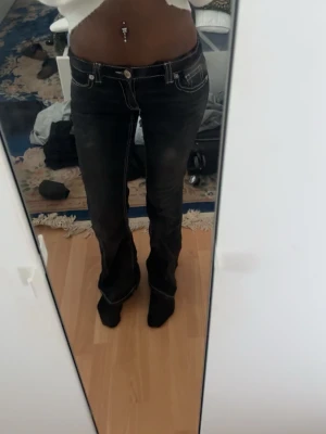 Svarta bootcut jeans med vita sömmar - Säljer ett par svarta bootcut jeans med tydliga vita kontrastsömmar och låg midja. Jeansen har klassiska fem fickor och utsvängda ben. Snygg detalj på bakfickorna. Perfekta för dig som gillar en retro vibe och vill sticka ut lite extra.