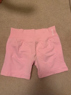 DFYNE rosa shorts - Säljer ett par ljusrosa shorts från DFYNE. De är tillverkade i ett stretchigt material som passar perfekt för träning. Shortsen har bred ribbad midja och en tight passform som ger en snygg siluett.