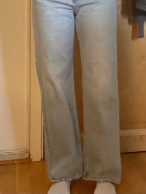 Ljusblå raka jeans med hög midja - Säljer ett par ljusblå jeans med raka ben och hög midja. Jeansen har klassisk femficksdesign och knäppning med flera knappar framtill. Perfekta för en avslappnad och trendig look. Materialet är denim i bomull.
