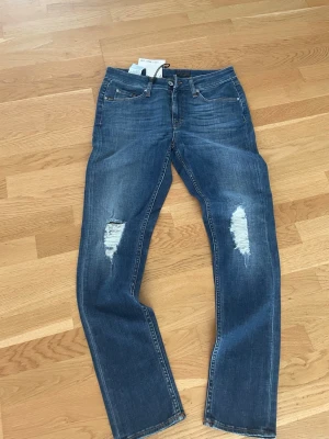 Blå slitna jeans med raka ben - Snygga blå jeans med raka ben och slitningar på båda knäna. Jeansen har klassisk femficksdesign och tydliga tvättade detaljer för en cool look. Perfekta för dig som gillar en avslappnad och trendig stil. Kontakta för frågor