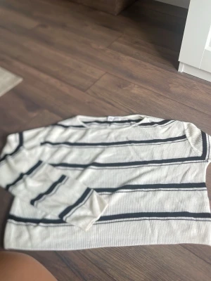 Vit stickad tröja med svarta ränder H&M - Säljer en vit stickad tröja från H&M med svarta horisontella ränder. Tröjan har rund halsringning och långa ärmar. Materialet är mjukt och ribbstickat, perfekt för en avslappnad och trendig look.