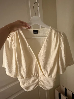 Krämvit omlottopp från Gina Tricot - Säljer en krämvit omlottopp från Gina Tricot med korta, vida ärmar och v-ringning. 