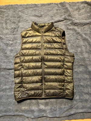 Ultra light down - Snygg olivgrön dunväst med hög krage och hel dragkedja framtill. Västen har ett quiltat mönster med horisontella sömmar och är tillverkad i glansigt material. Perfekt för lager-på-lager och ger en sportig look.